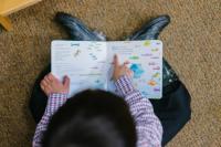 child sat on floor, reading tracing his finger across the pages