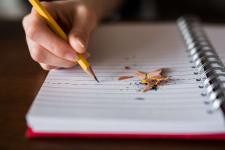 child writing in notebook, with a pencil, with pencil shavings next to writing