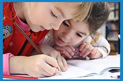 two children writing together, leaning over a book