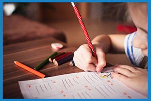 child writing or colouring on paper with coloured pencils