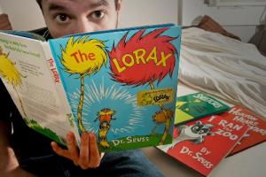 man reading the lorax, with dr seuss books piled next to him