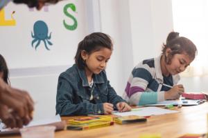 two children in bright lit classroom, writing in their books