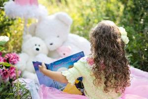 young girl reading to her teddy bears, outside on a blanket