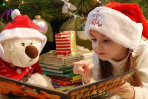 child reading book to her teddy bear, with christmas santa hats on