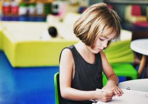 child in colourful classroom, writing in book