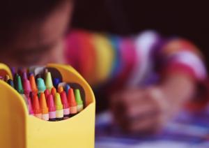 crayons in yellow pot, with a child colouring in the background