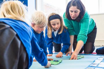 Founder Emma Ralph showing three children how to use the Mighty Writer resource on the floor